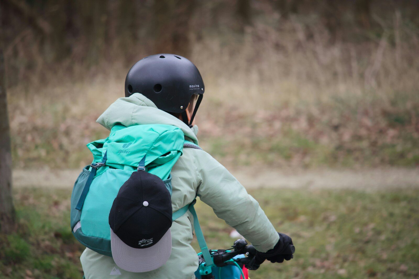 Barn med hjälm och ryggsäck cyklar på en gräsväg