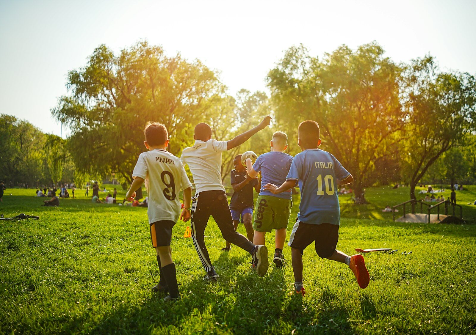 Barn spelar fotboll på en gräsplan i kvällssol